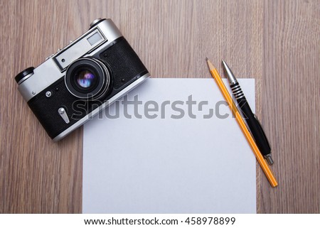 Old film camera with a white blank sheet and pen, pencil on wooden background