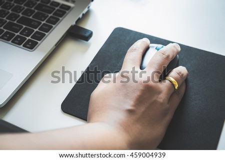 Woman hand clicking wireless mouse and working with the desktop computer while sitting at the office desk. Female using laptop to search for online e-commerce business data on table at the workplace.