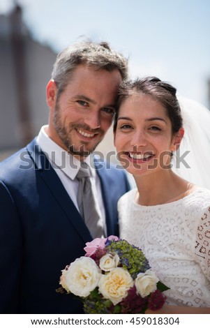 Portrait of newlyweds, smiling while they are looking at the camera, focus on the brunette bride