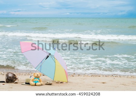 A bear doll wear bikini sitting with red hat and dry coconut on the beach in front of the sea