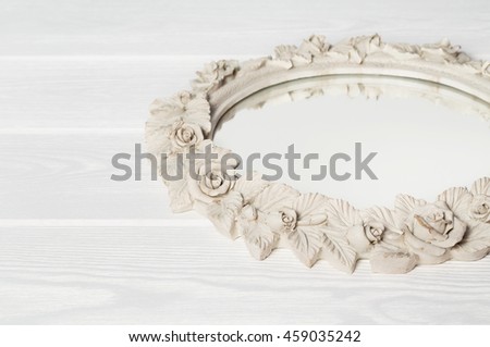 Still life shabby mirror with vintage floral round frame on a white wooden background closeup