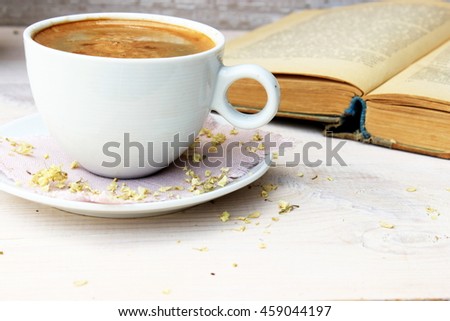 Full light composition with cup of hot tasty coffee, vintage book with yellow shabby cover and paper on white wooden background. Concept for beautiful romantic morning theme with retro decor elements
