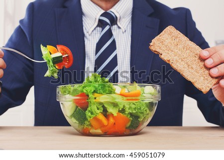 Man in suit unrecognizable torso eating healthy business lunch in modern office interior. Businessman at working place with vegetable salad in bowl, diet and right nutrition concept. Royalty-Free Stock Photo #459051079