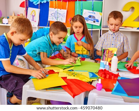 Children are making something out of colored paper on table in primary school. Children craft lesson in primary school. Development children craft at class in school.