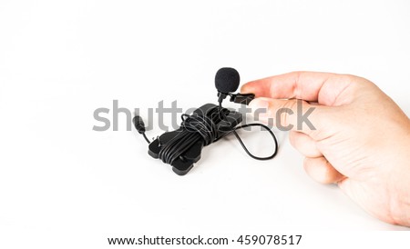 Close-up of a hand holding a tie-clip on microphone lapel or lavalier. Concept of sound recording or media broadcasting. Isolated on white background. Slightly de-focused and close-up shot. Copy space