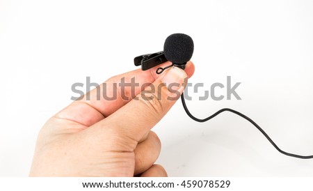 Close-up of a hand holding a tie-clip on microphone lapel or lavalier. Concept of sound recording or media broadcasting. Isolated on white background. Slightly de-focused and close-up shot. Copy space
