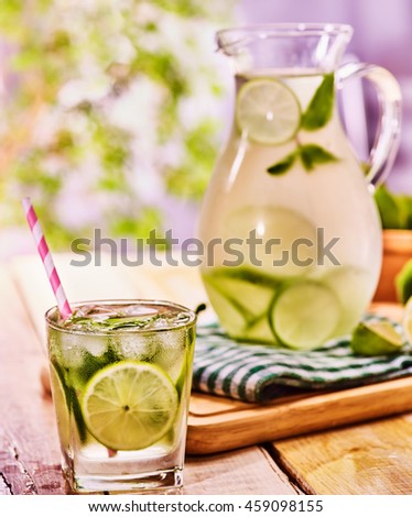 Country drink. On wooden boards is glass jug and glass with transparent drink and lime . Drink number two hundred seventy five with ice cubes . Country life. Light background. Healthy cocktail.