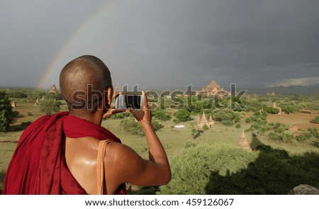 Monk in Bagan taking pictures to a rainbow