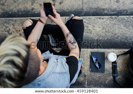 An upper view of stylish young woman using her cell phone while resting on stairs in the city.