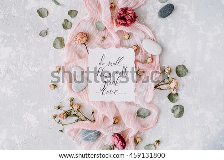 inspirational quote "do small things with great love" written in calligraphy style on paper with dry white tulips, eucalyptus petals and pink textile on concrete background. Flat lay, top view