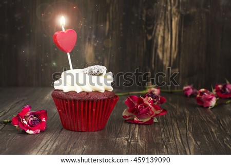 Delicious red velvet cupcake with burning candle. Anniversary, valentines day greeting card. Toned image. Selective focus