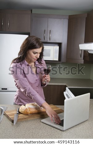 Young woman with a glass of wine and a house bread that has been cut, working on a laptop