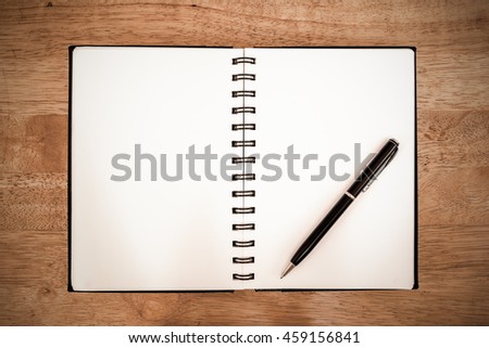 Dark vintage blank notebook page and pen on wood office table.Notepad with a pen on wooden background   
