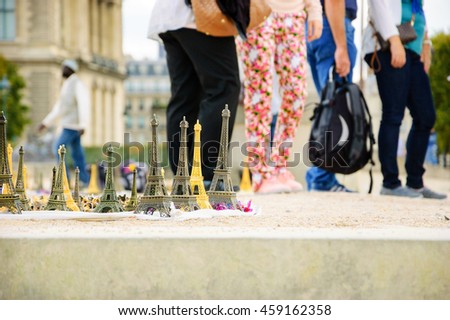 Eiffel tower statuettes for sale near Louvre museum and blurred figures of tourists at background.