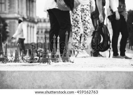 Eiffel tower statuettes for sale near Louvre museum and blurred figures of tourists at background. Black and white photo.