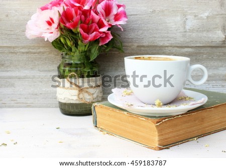 Full light composition with cup of fresh tasty coffee, vintage book with yellow shabby cover and paper and bouquet of pink flowers. Concept for romantic morning theme with retro decor elements