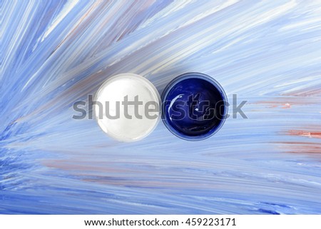 Creative concept with two jars of blue and white pigment over an abstract design of radiating blended streaks formed of the colors , overhead view