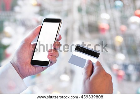 Business Man Hand Hold Smart phone or Cellphone with Credit Card over blurred Christmas Decorative background, Image for Solution of Mobile banking Shopping or Mobile Payment online concept.
