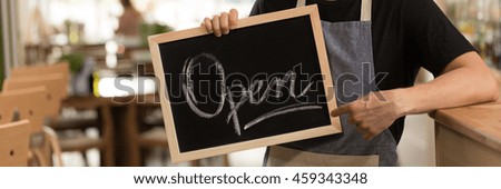 Close-up photo of a chalkboard with "open" written on it, in the hands of a barista in an apron