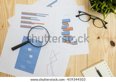Office workplace with Magnifying glass on wood table,supplies and reports for analysis business plan