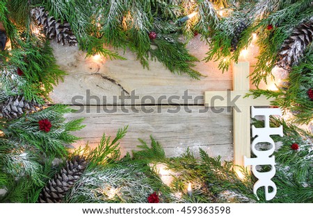 Christmas tree garland border with snow, wood cross, lights, and the word Hope, on antique rustic wooden background