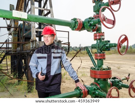 Oilfield worker near wellhead wearing red helmet and work clothes holding the radio. Oil and gas concept. 