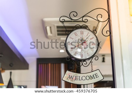 Old style hanging clock with welcome sign in coffee shop with bright sunlight,low light in shop