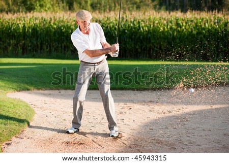 Mature or senior couple playing his ball out of a sand trap, ball in motion and lots of sand frozen (short shutter speed)