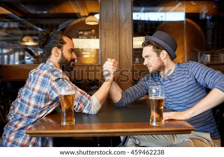 people, leisure, friendship and party concept - happy male friends drinking draft beer and arm wrestling at bar or pub and
