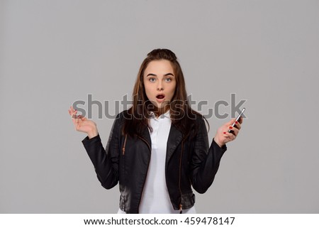 Surprised young beautiful girl holding phone over purple background. 