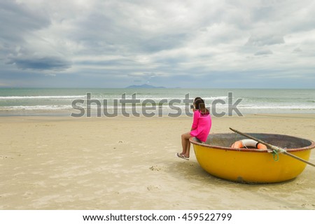 Woman sitting with her mobile phone on the Bamboo waterproof round fishing boat on the China Beach in Danang in Vietnam. It is also called Non Nuoc Beach. South China Sea  on the background.