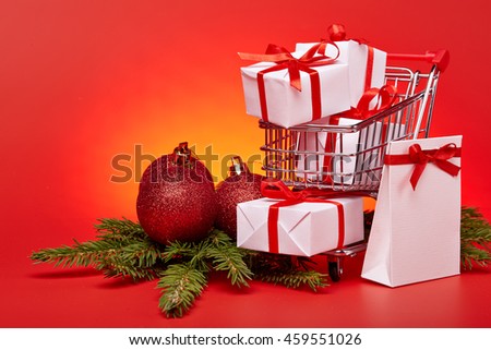 Shopping trolley with gift boxes and brenches of fir-tree with decoration on a red background. Christmas and New Year sale.