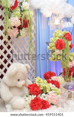 cute white teddy bear while surrounded by flowers,ornaments,gifts and ribbons 