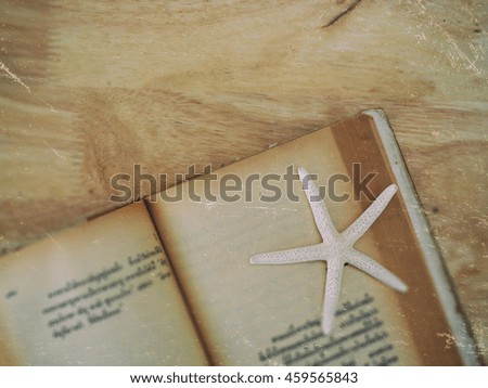 select focus of white finger starfish and old book page on wooden texture background with vintage color effect


