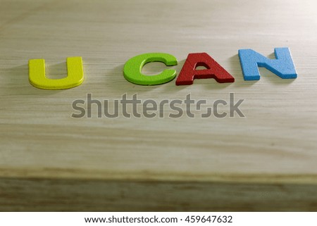Colourful alphabet with words U CAN on wooden table. One side is darker than the other side. Concept of possibility.