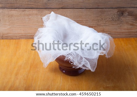 Clay pot with ghee under cheesecloth on light wooden table. Rustic still life. Royalty-Free Stock Photo #459650215