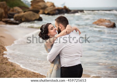 Wedding. Wedding by the sea. Couple in love after a walk along the beach hugging each other. Kiss on background of the sea, beach, cliffs after wedding ceremony. Beautiful sea surf and true emotions.