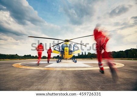 Alarm for the air rescue service. Team of rescuers (paramedic, doctor and pilot) running to the helicopter on the heliport. Royalty-Free Stock Photo #459726331