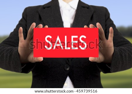 Businesswoman in a black jacket shows a card with the inscription sales. Selective focus.