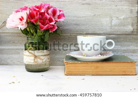 Full light composition with cup of fresh tasty coffee, vintage book with yellow shabby cover and paper and bunch of pink flowers. Concept for beautiful romantic morning theme with retro decor elements