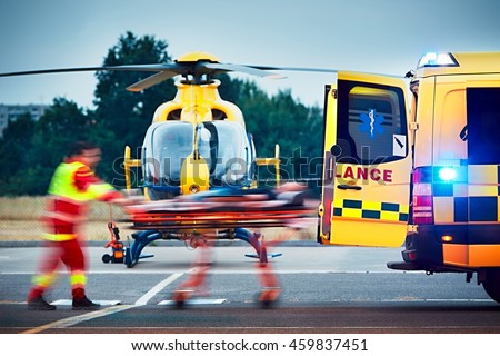 Cooperation between air rescue service and emergency medical service on the ground. Paramedic is pulling stretcher with patient to the ambulance car. Royalty-Free Stock Photo #459837451
