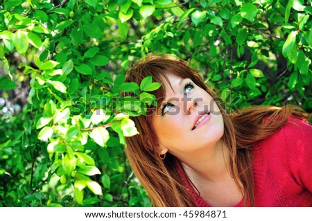 redheaded girl through green leaves in spring time