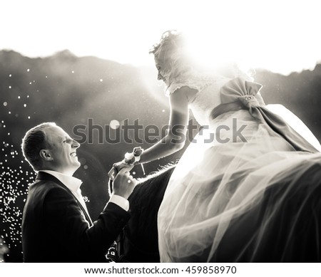 Black and white picture of a bride reaching her hand to a groom while she sits on the horse
