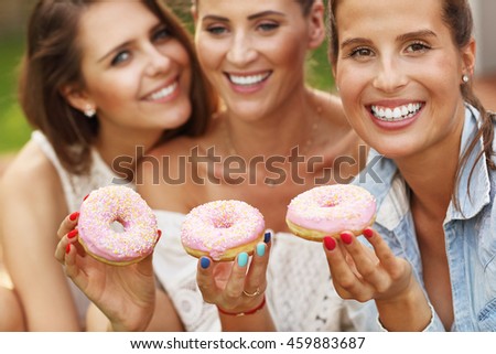 Picture presenting happy group of friends eating donuts outdoors