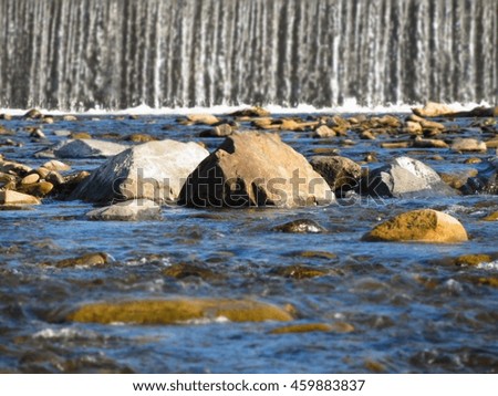 photo of blue river with some stones and a weir at the background with foreground and background blurred
