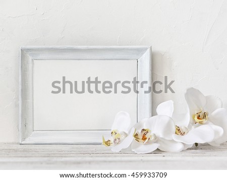 White photo frame with white orchids on the vintage table. Wedding decoration with text space. Frame for quotes.