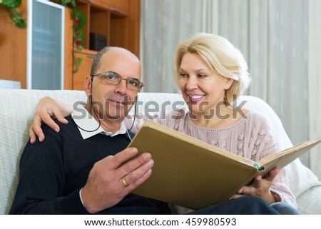 Happy elderly husband and wife sitting on couch with photograph album