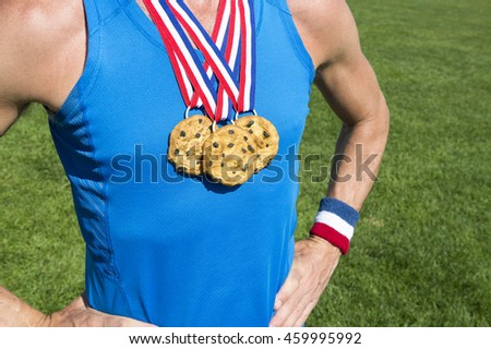 Athlete wearing chocolate chip cookies gold medals standing in front of green grass playing field background