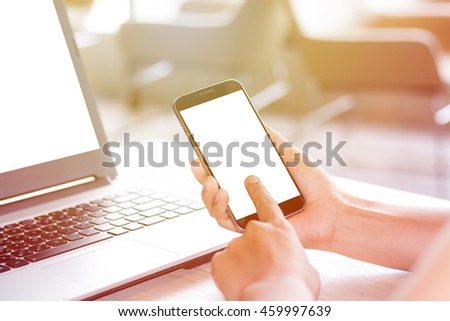 Close Up of woman's hands using mobile phone and laptop computer with blank copy space screen for your advertising text message or content, in the morning light.