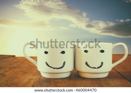 coffee cup with happy faces over wooden table in front of blue sky. vintage filtered. happy weekend concept